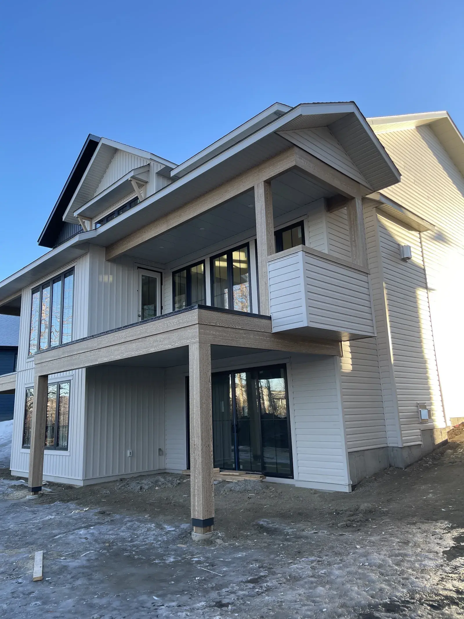 Two-storey new build in a Red Deer subdivision with cream lap siding, charcoal board-and-batten gables and black-framed windows, finished by PJM Home Advantage